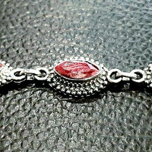 May include: A silver bracelet with three red gemstone accents. The gemstones are set in a silver bezel and surrounded by small silver beads.