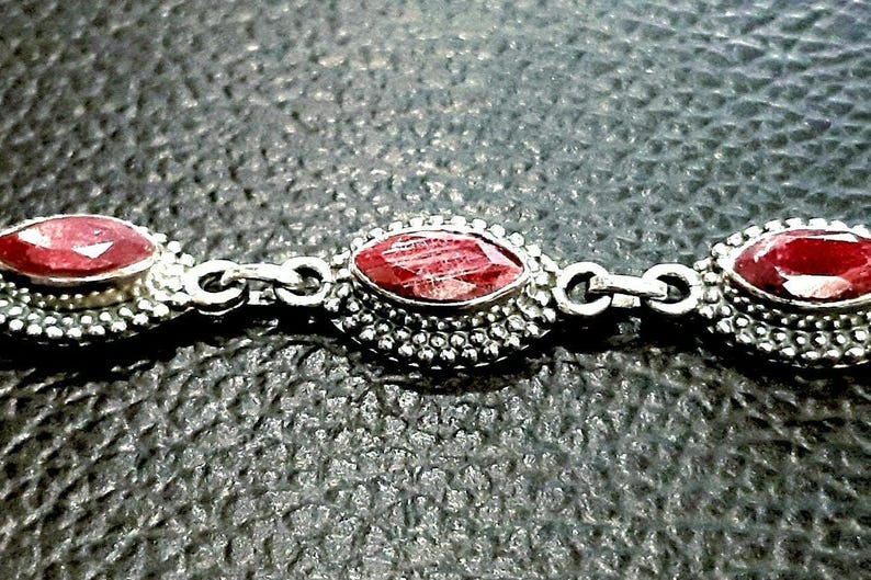 May include: A silver bracelet with three red gemstone accents. The gemstones are set in a silver bezel and surrounded by small silver beads.
