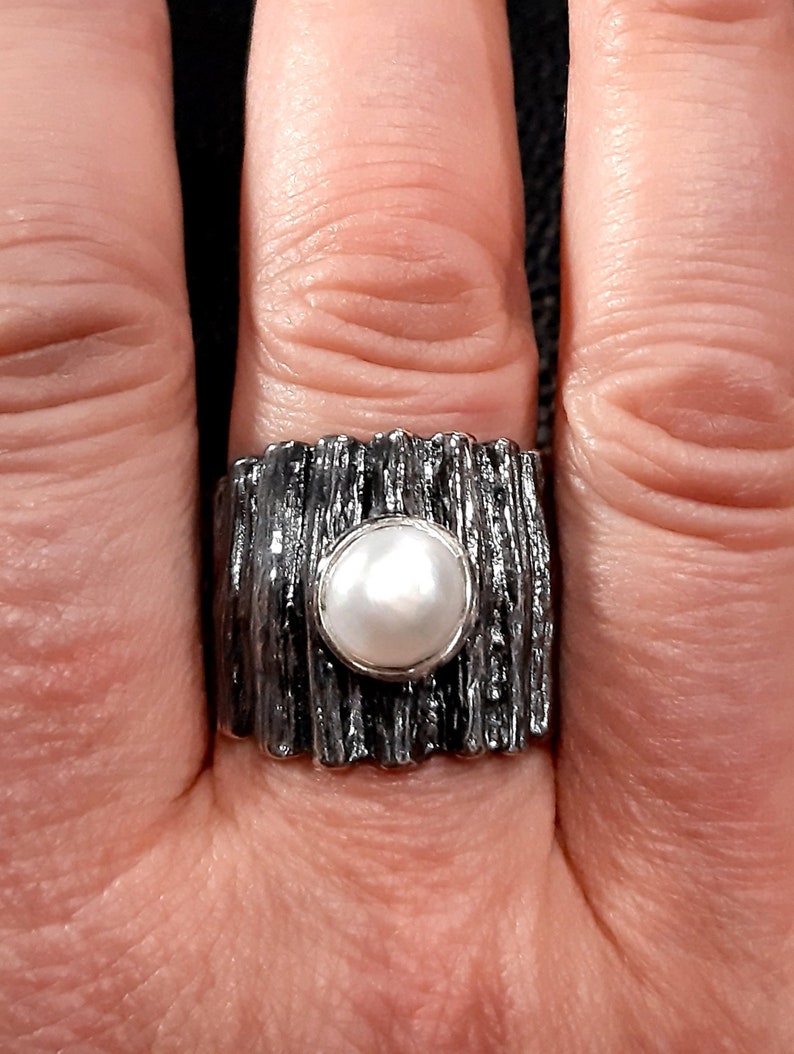 May include: A silver ring with a textured band and a white pearl in the center.