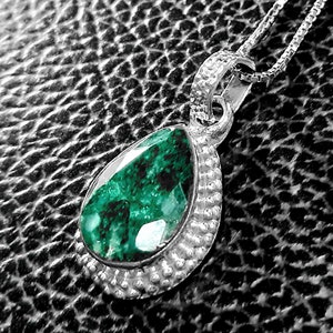May include: A silver pendant necklace with a teardrop-shaped green gemstone set in a silver bezel. The pendant is surrounded by a beaded border.