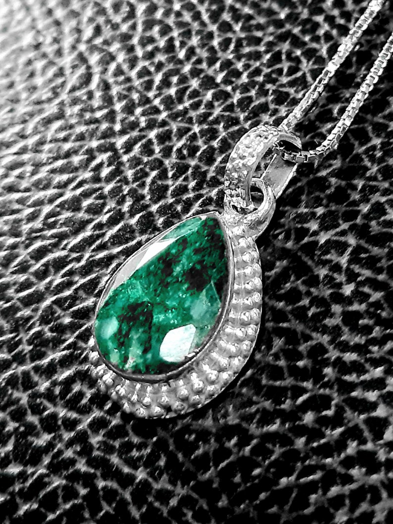 May include: A silver pendant necklace with a teardrop-shaped green gemstone set in a silver bezel. The pendant is surrounded by a beaded border.