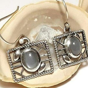 May include: A pair of silver earrings with a gray stone set in a geometric design.