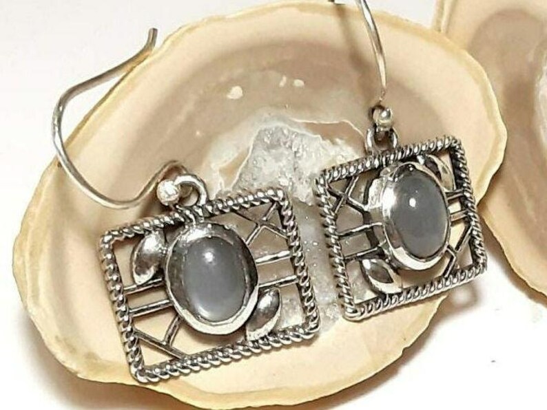 May include: A pair of silver earrings with a gray stone set in a geometric design.