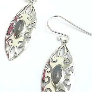 May include: A pair of silver earrings with a delicate filigree design and a gray gemstone in the center of each earring.