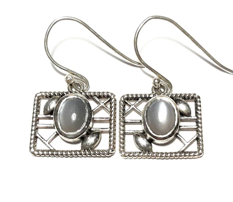 May include: A pair of silver earrings with a gray moonstone in a geometric design.