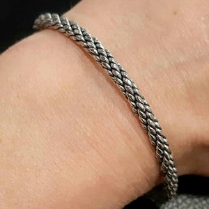 May include: A silver braided bangle bracelet on a person's wrist.