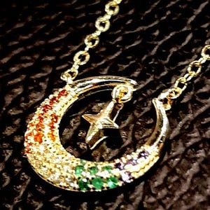 May include: A gold crescent moon necklace with a star charm. The moon is decorated with colorful gemstones.