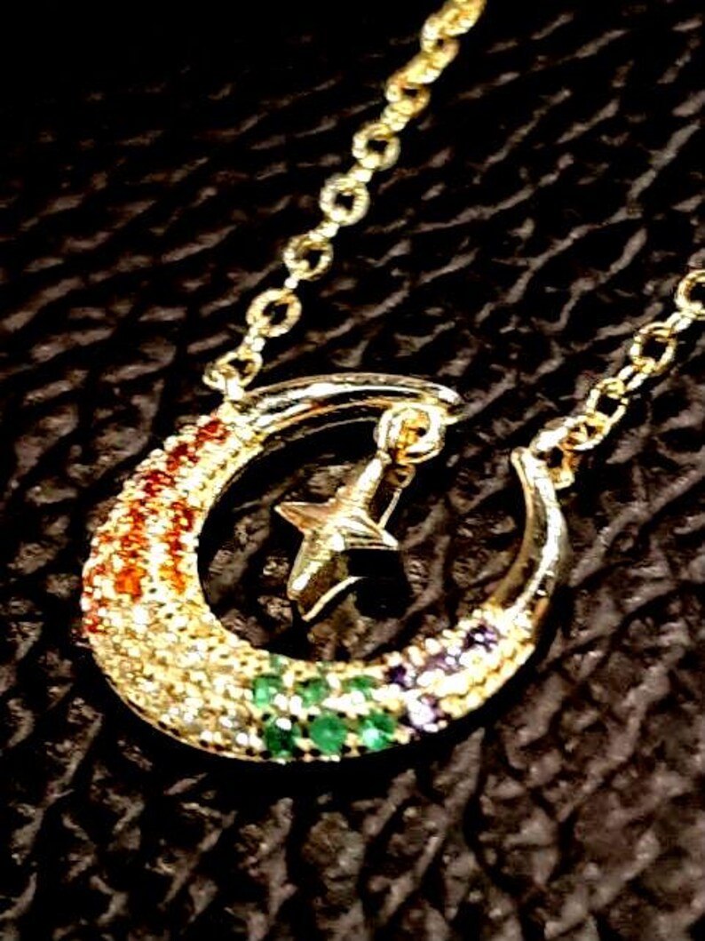 May include: A gold crescent moon necklace with a star charm. The moon is decorated with colorful gemstones.