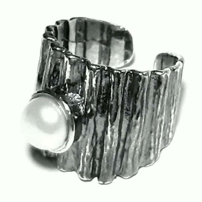 May include: A silver ring with a textured, ridged band and a large, white pearl set in the center.