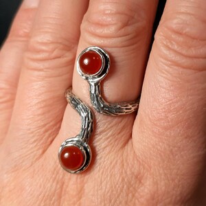 May include: A silver ring with a textured, branch-like design. The ring has two red carnelian stones set in the design.