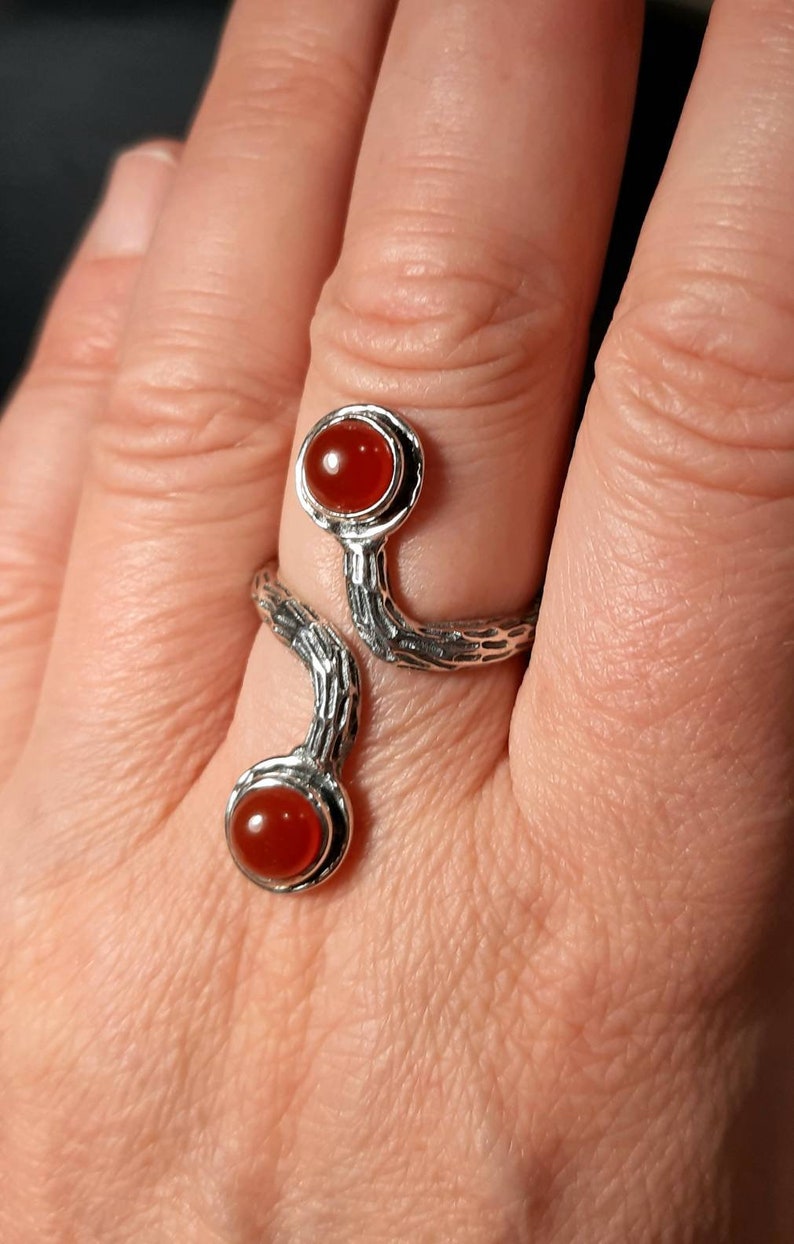 May include: A silver ring with a textured, branch-like design. The ring has two red carnelian stones set in the design.