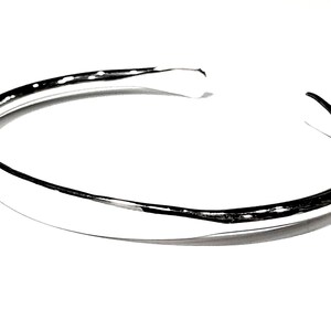 May include: A silver bangle bracelet with a smooth, rounded surface.