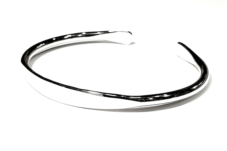 May include: A silver bangle bracelet with a smooth, rounded surface.