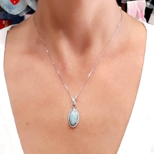May include: A silver chain necklace with a light blue gemstone pendant. The pendant is oval shaped and has a silver border.