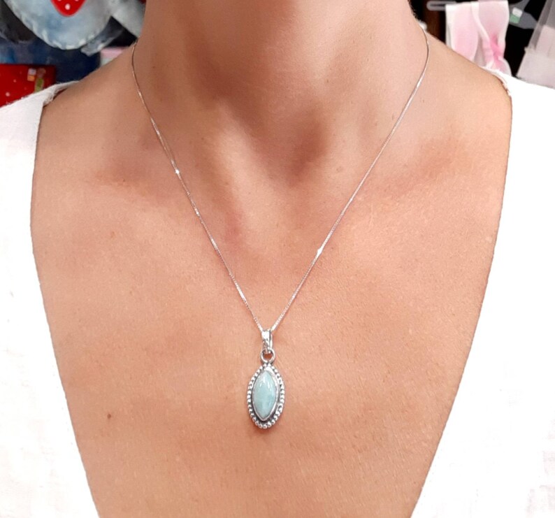 May include: A silver chain necklace with a light blue gemstone pendant. The pendant is oval shaped and has a silver border.
