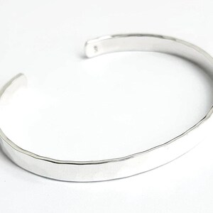 May include: A silver hammered bangle bracelet. The bracelet is simple and elegant, with a smooth, polished finish.