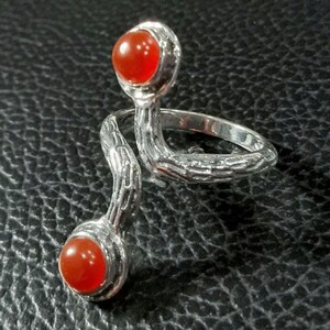 May include: A silver ring with two orange carnelian stones. The ring is designed to wrap around two fingers.