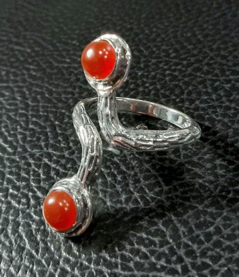 May include: A silver ring with two orange carnelian stones. The ring is designed to wrap around two fingers.