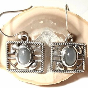 May include: A pair of silver earrings with a gray gemstone set in a silver frame. The frame has a delicate, intricate design.