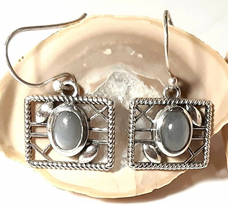 May include: A pair of silver earrings with a gray gemstone set in a silver frame. The frame has a delicate, intricate design.