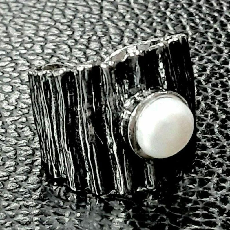 May include: A silver ring with a textured, wood-like band and a large, white pearl set in the center.