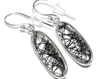 May include: A pair of silver earrings with clear, oval-shaped stones. Each stone has a network of black, linear inclusions. The earrings have a hook design with clear, plastic stoppers.