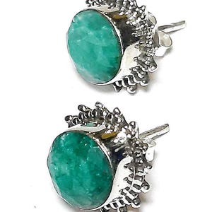 Puede incluir: Un par de pendientes de bot&oacute;n con piedras preciosas redondas de color verde vibrante engastadas en metal plateado. El metal tiene un dise&ntilde;o texturizado y puntiagudo alrededor de la piedra preciosa. Los pendientes se muestran sobre un fondo blanco.
