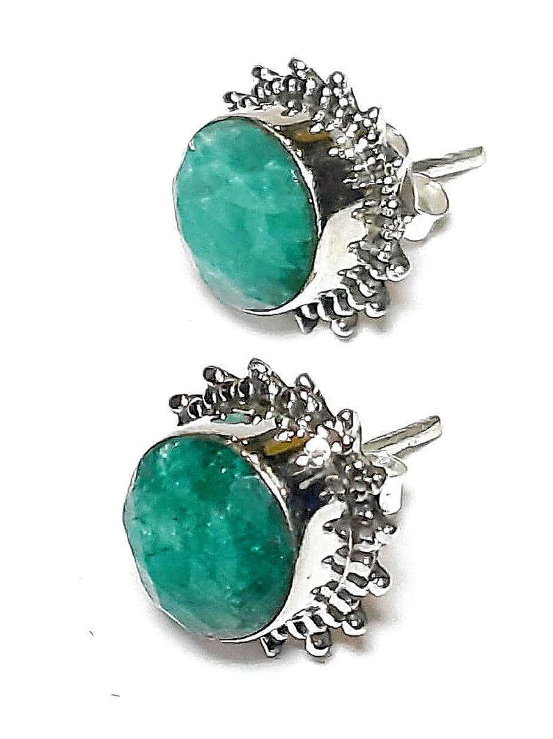 Puede incluir: Un par de pendientes de bot&oacute;n con piedras preciosas redondas de color verde vibrante engastadas en metal plateado. El metal tiene un dise&ntilde;o texturizado y puntiagudo alrededor de la piedra preciosa. Los pendientes se muestran sobre un fondo blanco.