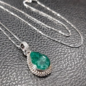 May include: A silver necklace with a teardrop-shaped emerald pendant. The pendant is set in a silver bezel and has a textured edge.