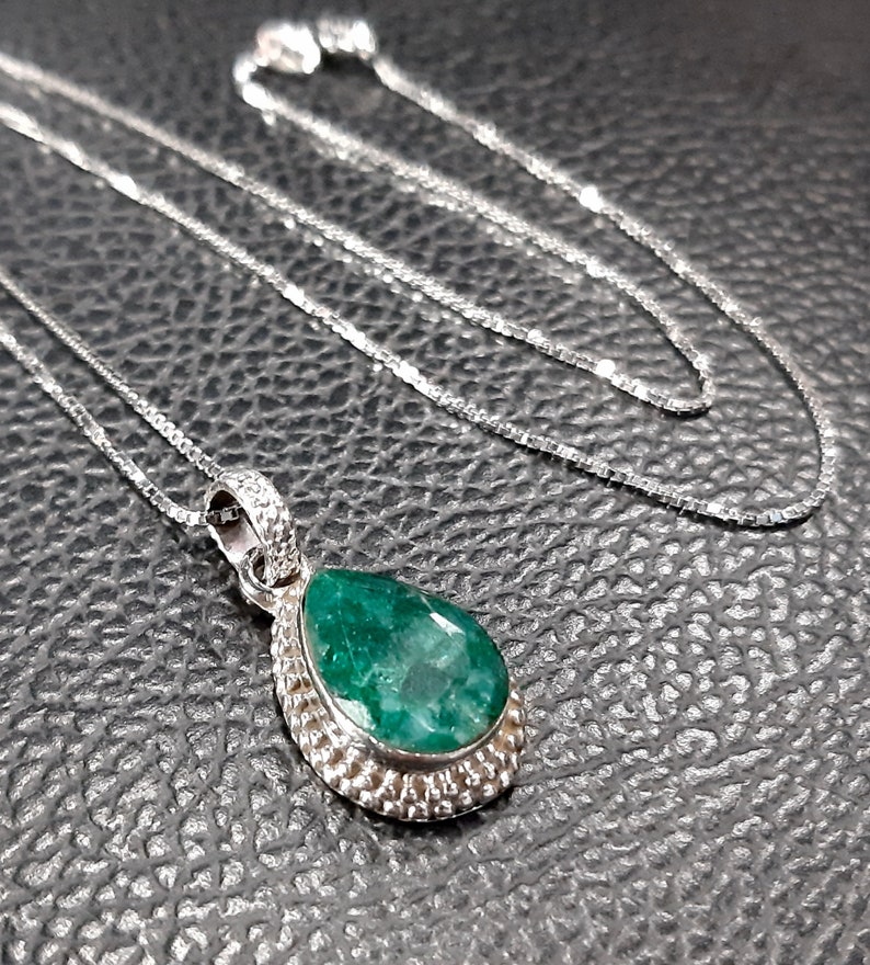 May include: A silver necklace with a teardrop-shaped emerald pendant. The pendant is set in a silver bezel and has a textured edge.