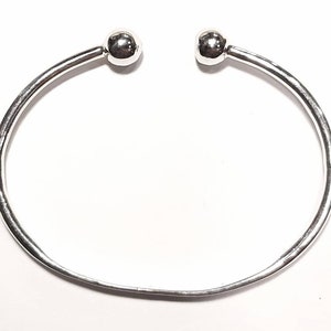 Op de afbeelding: Een zilveren armband met twee ronde bolletjes aan de uiteinden.