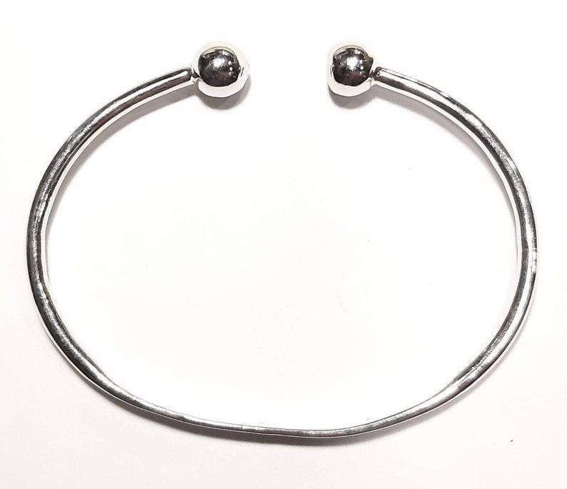 Op de afbeelding: Een zilveren armband met twee ronde bolletjes aan de uiteinden.