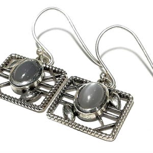 May include: A pair of silver earrings with a gray stone set in a geometric design.