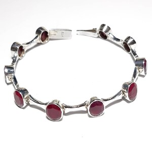 May include: A silver bracelet with red gemstones. The bracelet has a clasp closure and is made of sterling silver.
