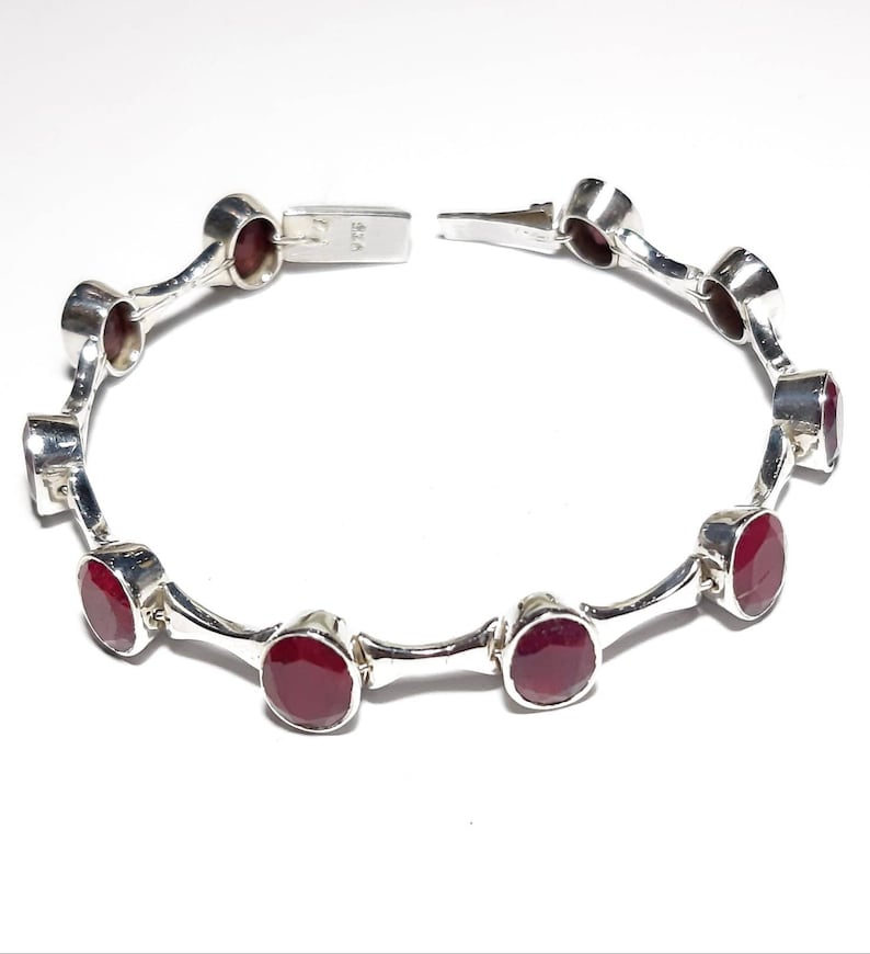 May include: A silver bracelet with red gemstones. The bracelet has a clasp closure and is made of sterling silver.