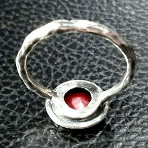 Pu&ograve; includere: Un anello d'argento con una pietra preziosa rossa incastonata in una montatura a castone. La fascia dell'anello &egrave; martellata e ha una finitura testurizzata.