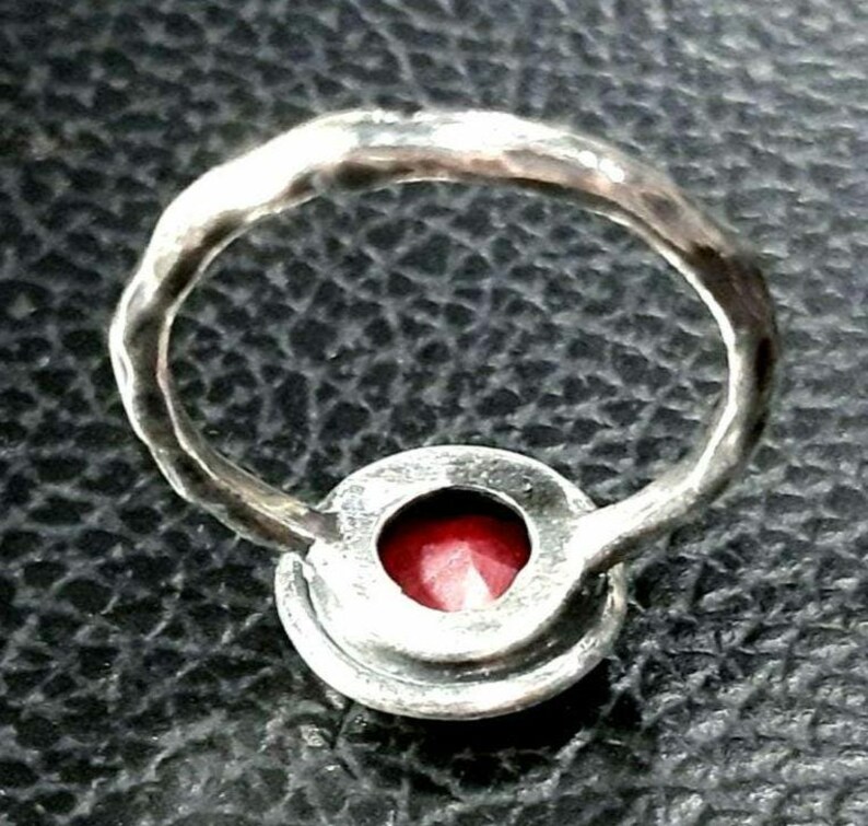 Pu&ograve; includere: Un anello d'argento con una pietra preziosa rossa incastonata in una montatura a castone. La fascia dell'anello &egrave; martellata e ha una finitura testurizzata.