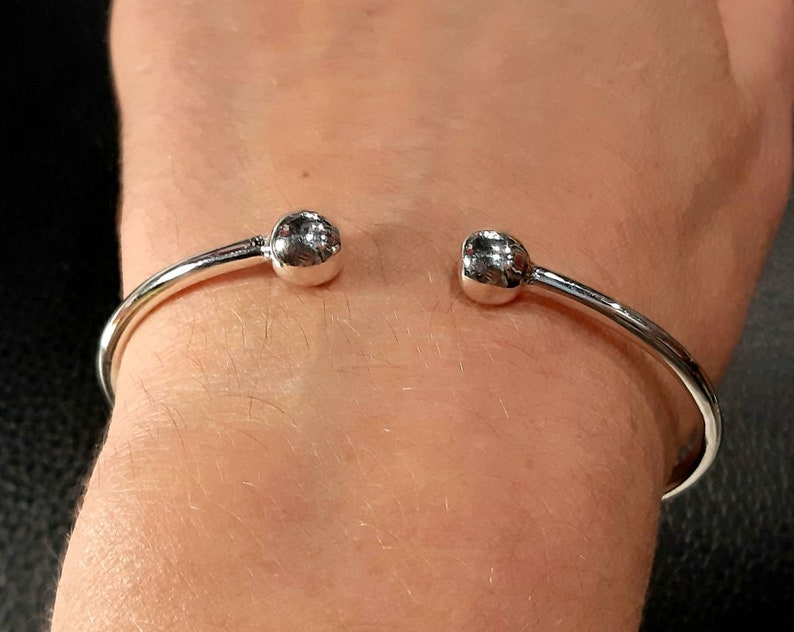Op de afbeelding: Een zilveren armband met twee ronde, gladde zilveren ballen aan de uiteinden.