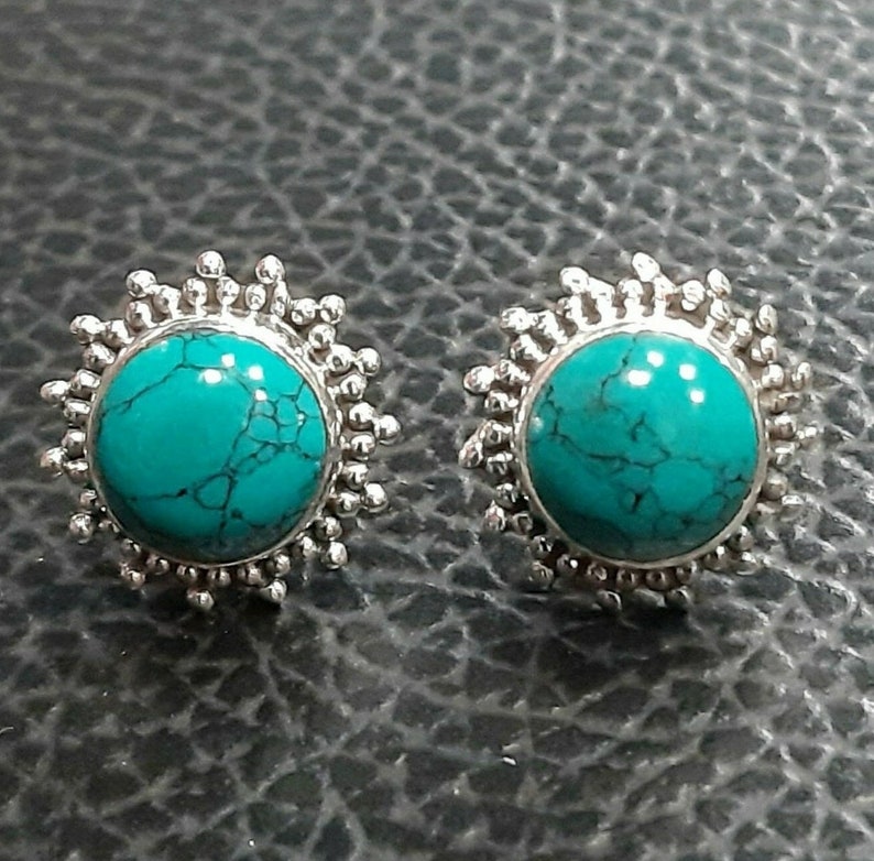 K&ouml;nnte beinhalten: Ein Paar silberne Ohrringe mit t&uuml;rkisfarbenen Steinen, die in einem Sonnenstrahl-Design eingefasst sind.