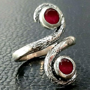 Puede incluir: Un anillo de plata con un diseño texturizado en forma de serpiente. El anillo tiene dos piedras preciosas rojas engastadas en el diseño.