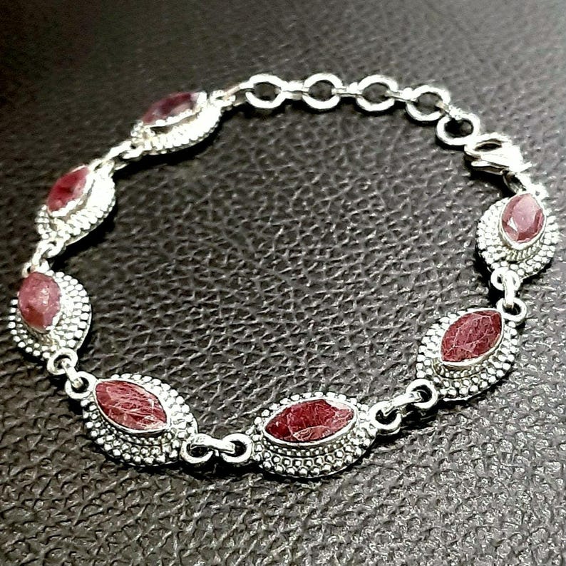 May include: A silver bracelet with a chain link design and six oval-shaped red gemstones. The gemstones are set in silver bezels and have a textured surface.