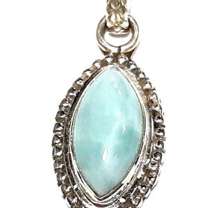 May include: A silver pendant with a light blue marquise-shaped gemstone set in a beaded border.