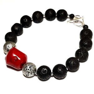 Puede incluir: Un brazalete de cuentas de lava negra y coral rojo con un cierre de palanca plateado.