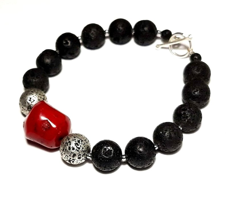 Puede incluir: Un brazalete de cuentas de lava negra y coral rojo con un cierre de palanca plateado.