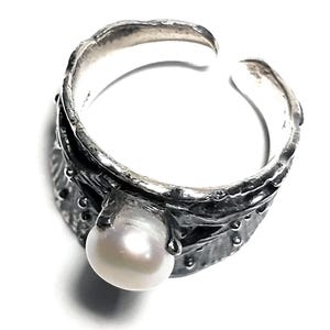 May include: A silver ring with a textured band and a white pearl. The ring is open and adjustable.