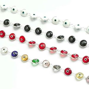 May include: Five silver bracelets with different colored evil eye charms. The charms are round and have a silver rim. The bracelets are all laid out in a row on a white surface.