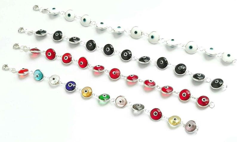 May include: Five silver bracelets with different colored evil eye charms. The charms are round and have a silver rim. The bracelets are all laid out in a row on a white surface.