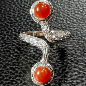 May include: A silver ring with a twisted band and two round carnelian gemstones. The ring has a textured, tree bark-like design.