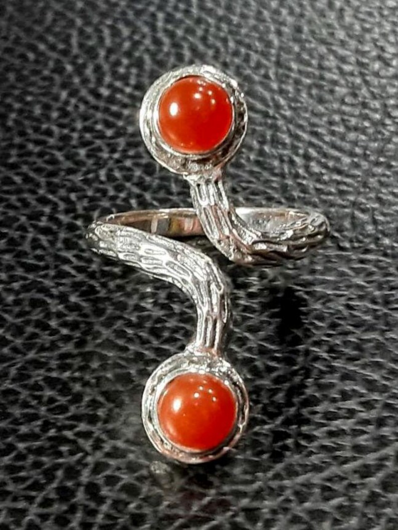 May include: A silver ring with a twisted band and two round carnelian gemstones. The ring has a textured, tree bark-like design.