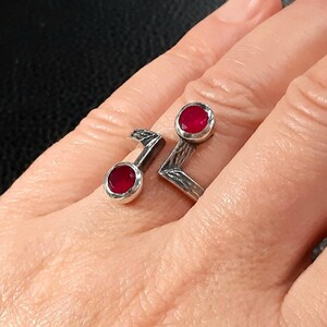 Peut inclure: Une bague en argent avec deux pierres précieuses rouges serties dans la bande. La bague est conçue en forme de note de musique.